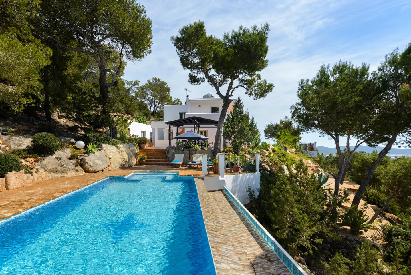 Exterior view of a white house with a pool, trees, and blue sky.
