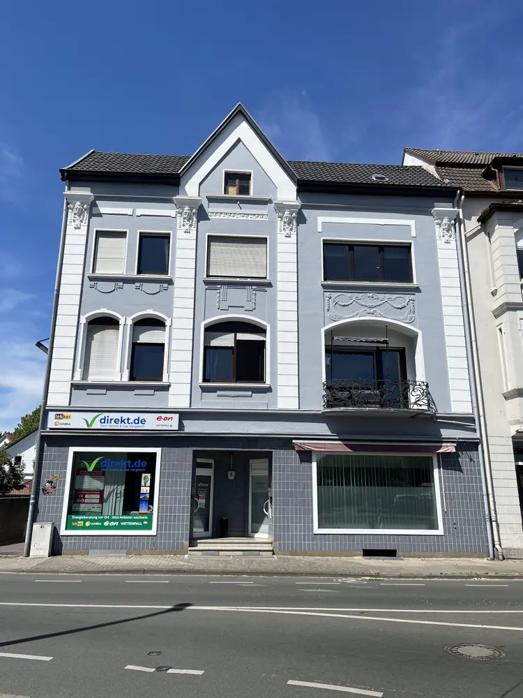 Three-story light blue building with white trim and dark windows under a clear blue sky. A "direkt.de" sign is visible on the ground floor.
