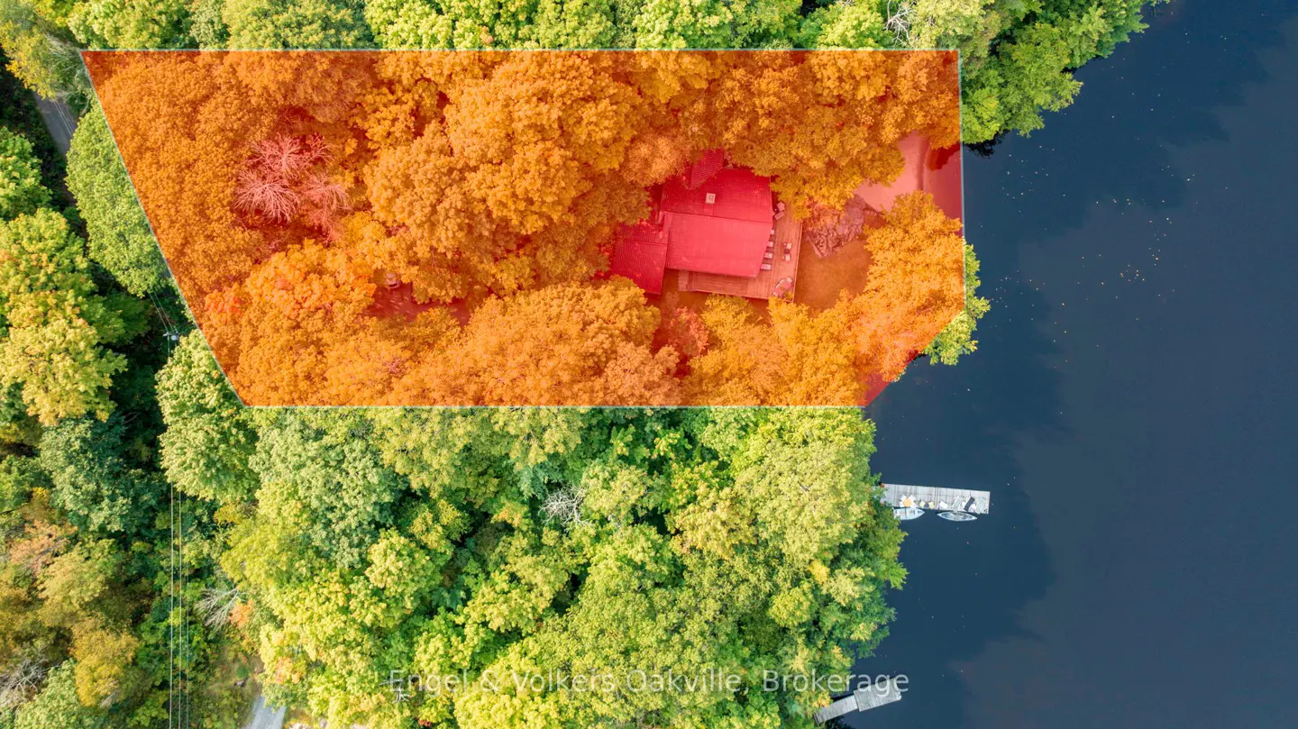 Aerial view of a property with a red roof, surrounded by orange and green trees, next to a lake with a dock.