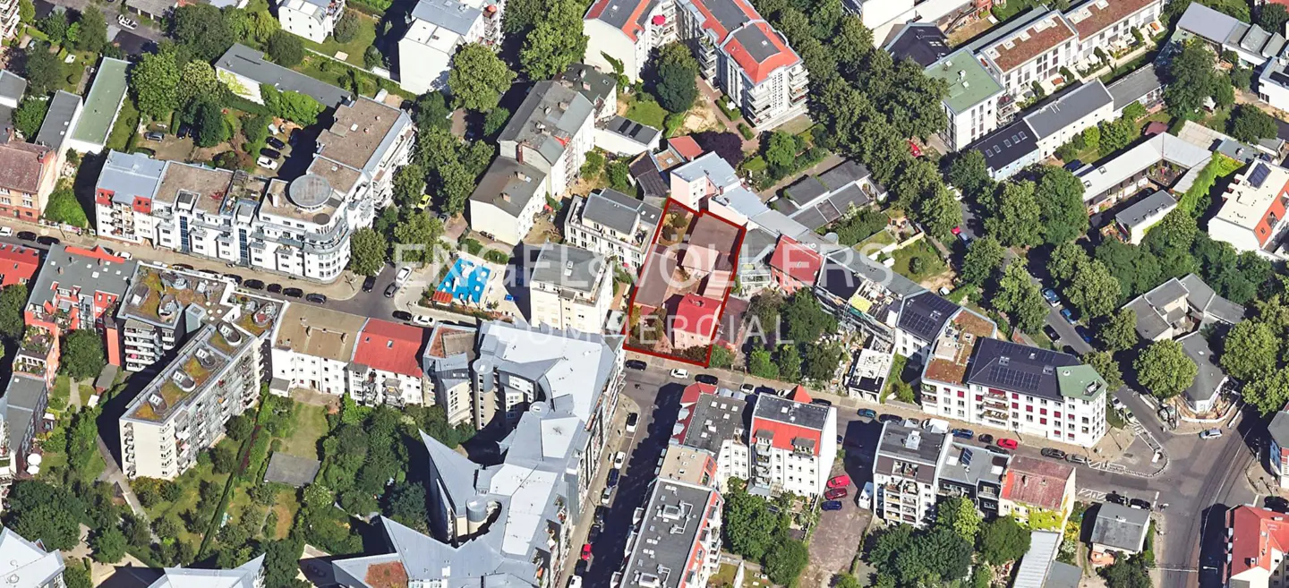 Aerial view of a city neighborhood with buildings, trees, and streets. A building is outlined in red.