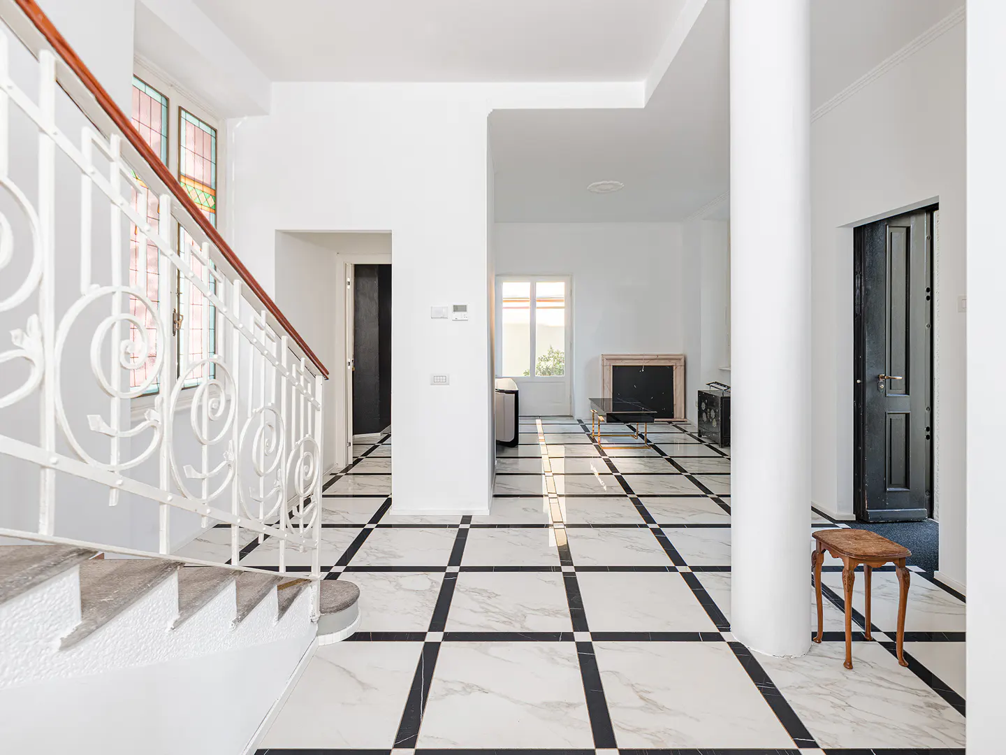 Bright foyer with white marble floors featuring black grid patterns, a white staircase, a central pillar, and a fireplace.