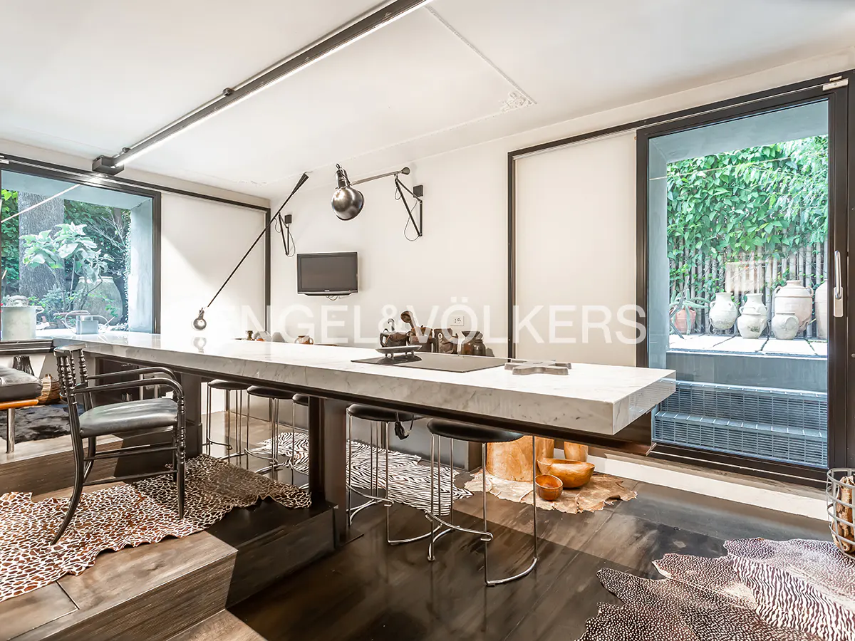 Modern interior with a long marble table, black stools, and animal print rugs. A sliding glass door leads to a green outdoor space.