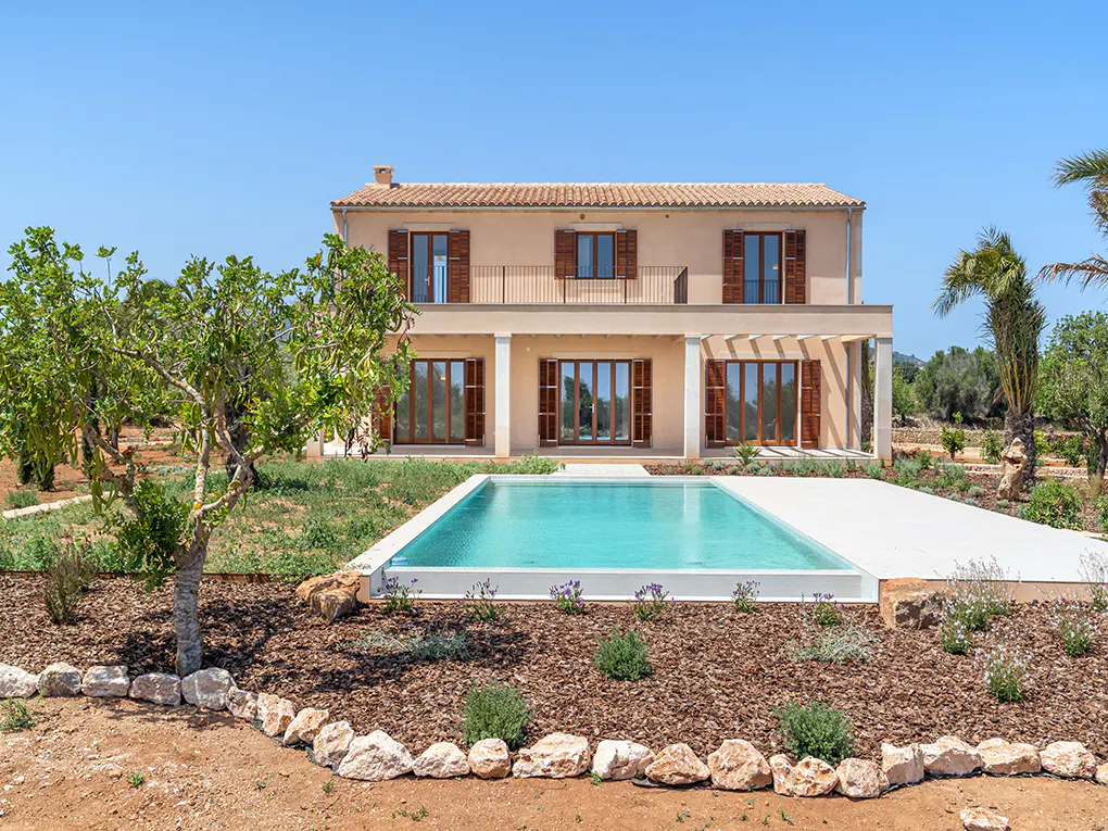 Two-story beige house with brown shutters, a red tile roof, and a turquoise pool in the front yard.