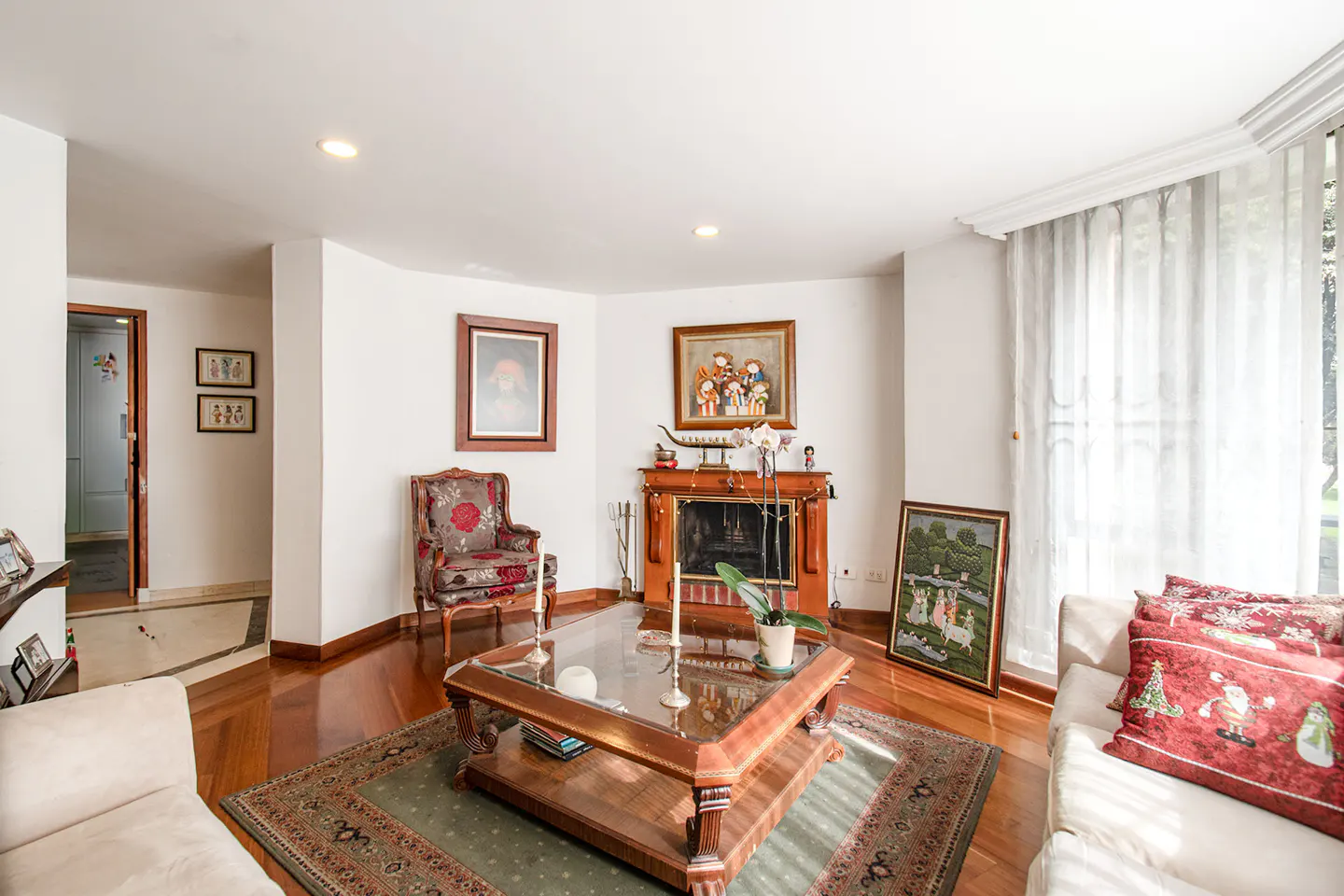 Living room with a wooden fireplace, glass coffee table, patterned armchair, and white sofas on a green area rug.