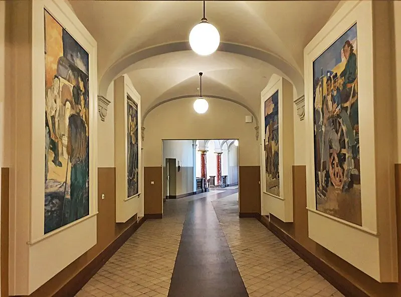 Hallway with arched ceiling, globe lights, and large framed paintings on the walls. The floor is tiled with a dark runner.