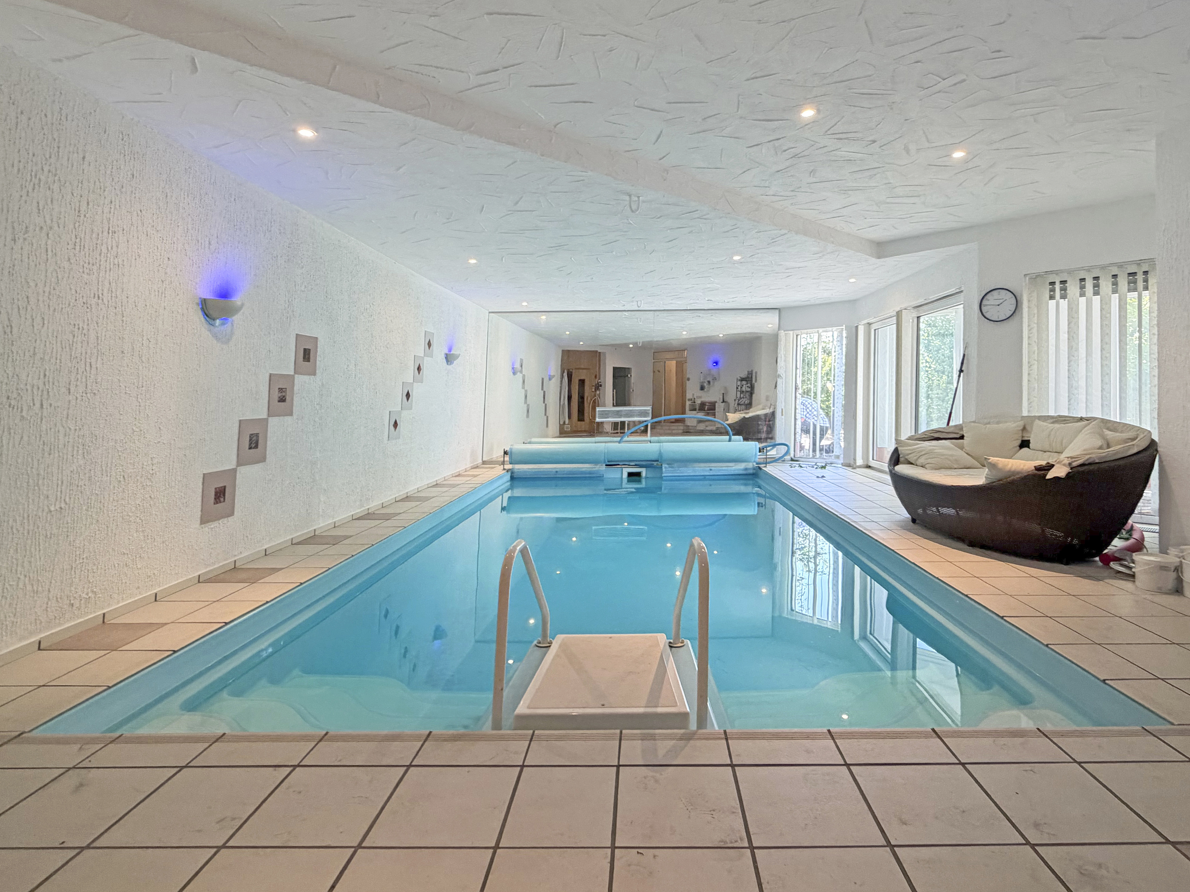 Indoor swimming pool with blue water, tiled floor, a curved lounge chair, and blue accent lighting on white walls. [AI-generated text]