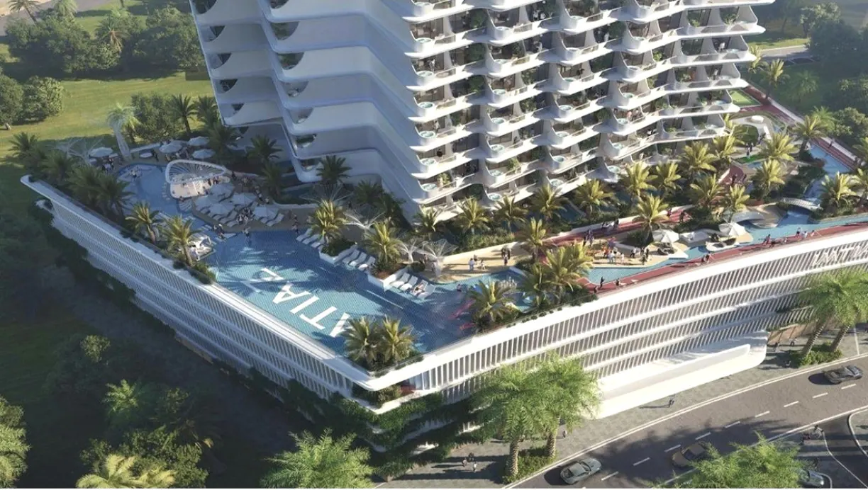 Aerial view of a modern white high-rise building with a large swimming pool, palm trees, and lounge areas on the terrace.