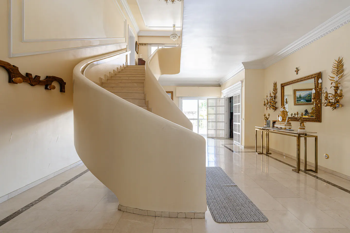 Bright foyer with a curved staircase, marble floors, and a gold console table with a mirror.