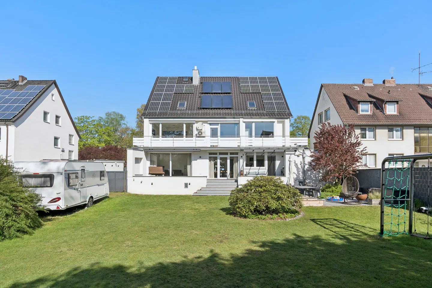 Two-story white house with solar panels, a green lawn, and a camper parked on the side.
