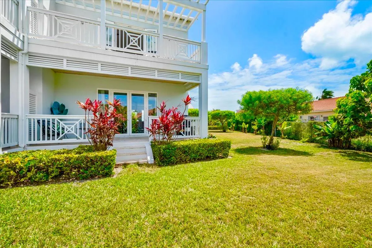 Two-story white building with a balcony overlooking a green lawn and trees under a blue sky.