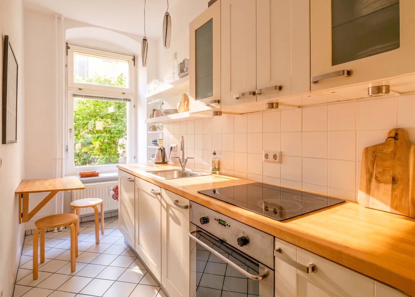 Bright kitchen with white cabinets, wood countertop, and stainless steel appliances. A window overlooks a green garden.