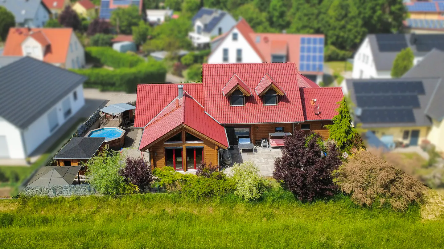 A high angle shot of a house with a red roof, a pool, and green grass in the foreground.