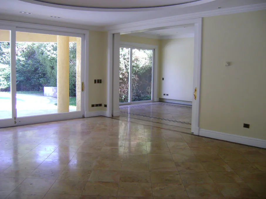 An interior shot of a bright, empty room with beige walls and marble tile flooring. Sliding glass doors lead to a green outdoor space.