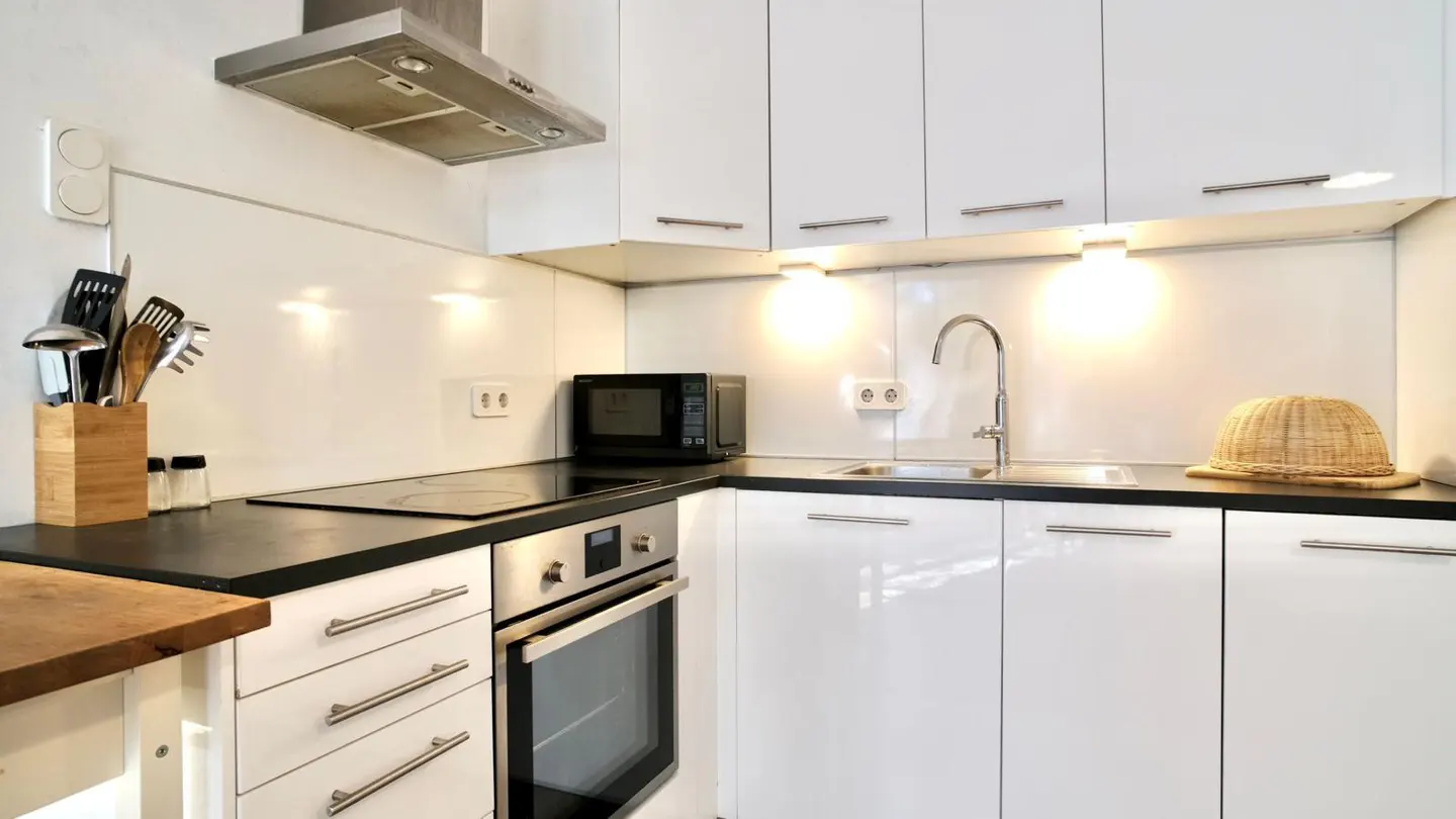 Bright kitchen with white cabinets, black countertops, and stainless steel appliances. A woven hat sits near the sink.