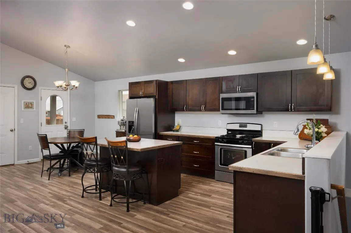 A bright kitchen with dark wood cabinets, stainless steel appliances, and a center island with bar stools. A round table sits near a white door.