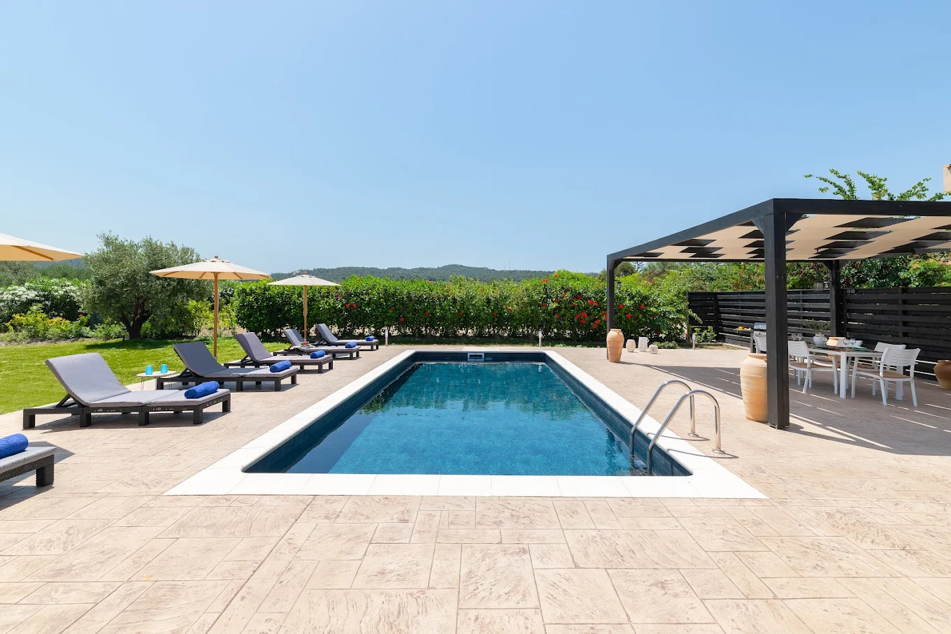 Rectangular swimming pool on a stone patio with lounge chairs, umbrellas, and a shaded dining area under a pergola. [AI-generated text]