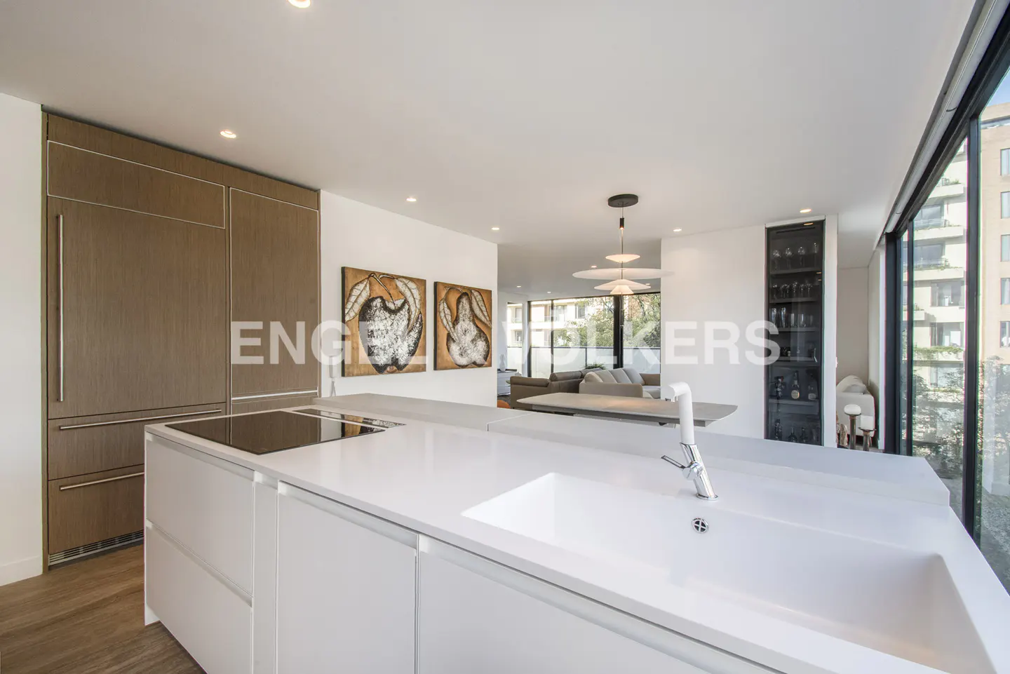 A modern kitchen with white cabinets, a large island with a sink, and stainless steel appliances. Artwork hangs on the wall.