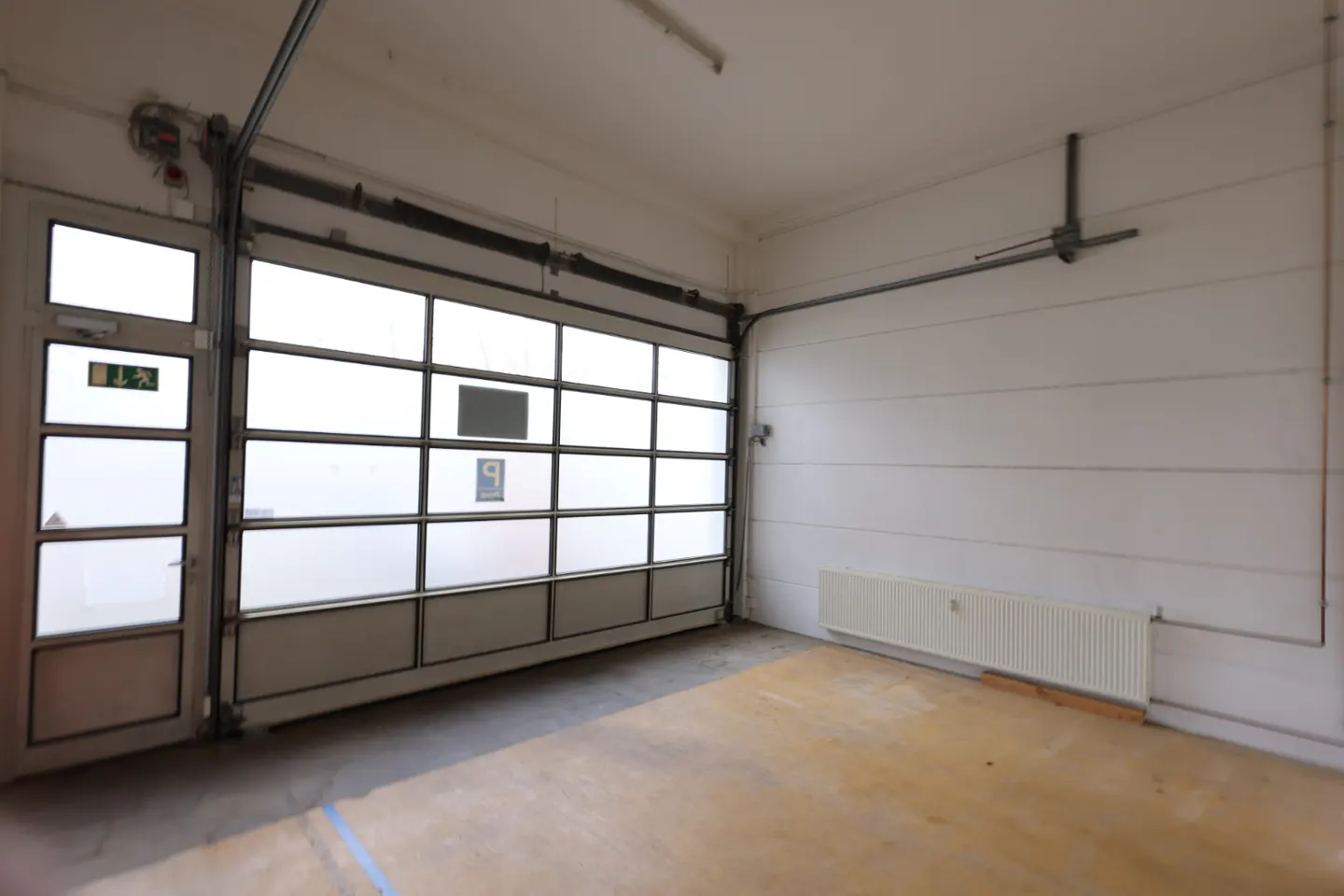 Empty white garage with a large sectional door and a smaller exit door on the left. A radiator is on the right wall.