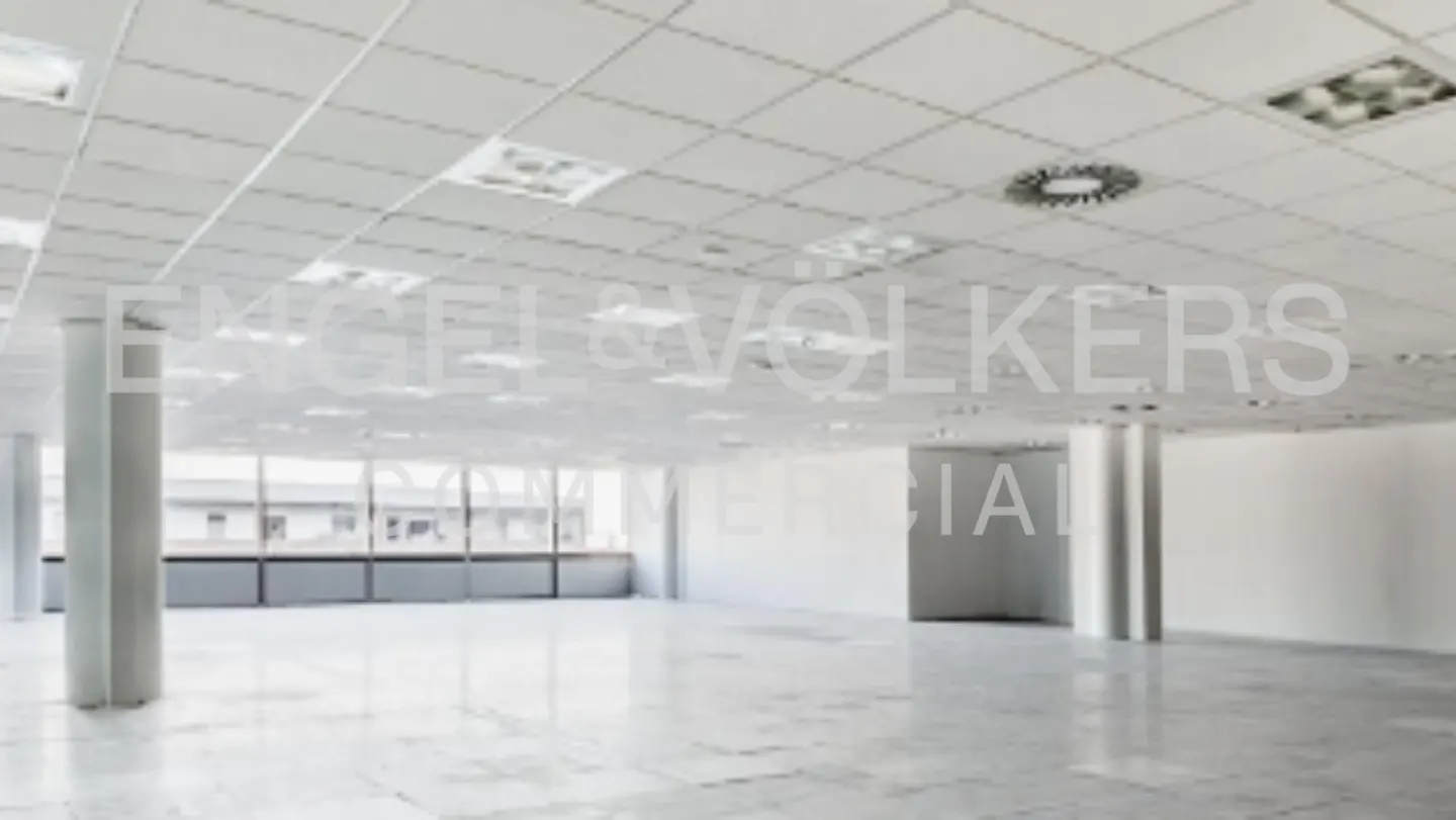 An empty, bright commercial space with white walls, columns, and a tiled floor. Large windows line one side of the room.