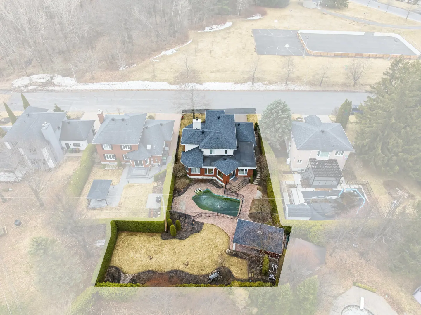 Aerial view of a red brick and white two-story house with a pool and a large yard.