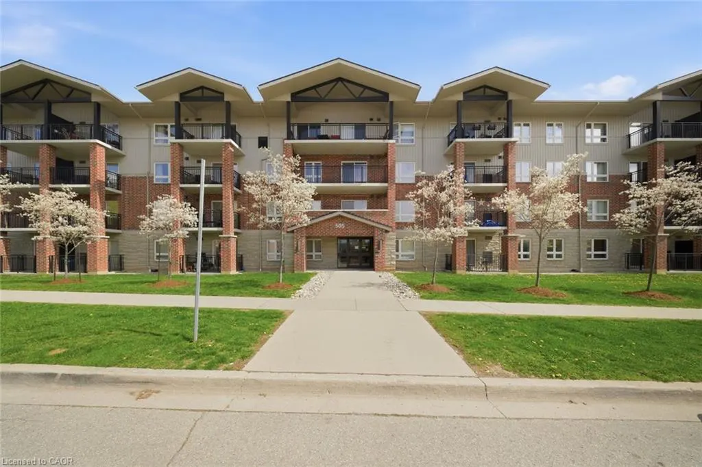 Exterior view of a three-story apartment building with balconies, brick pillars, and a green lawn.