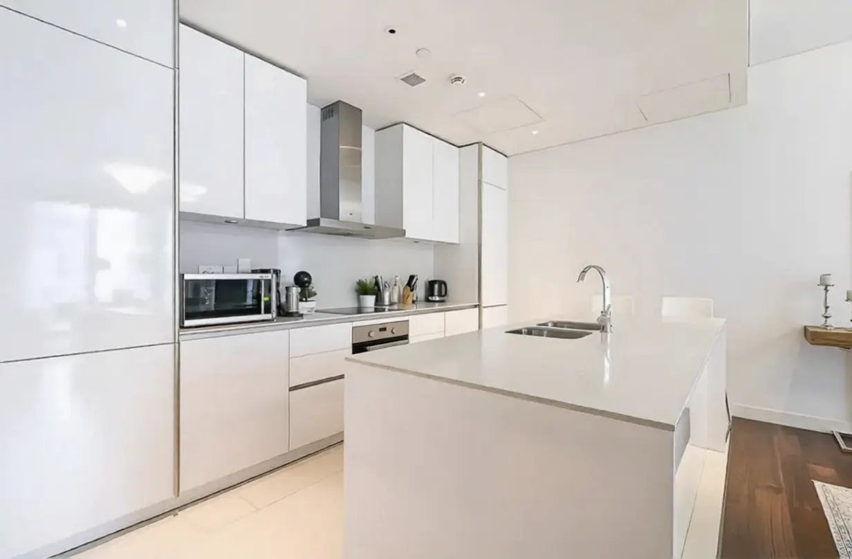 Bright, modern kitchen with white cabinets, stainless steel appliances, and a large island with a sink. Dark wood floors add contrast.