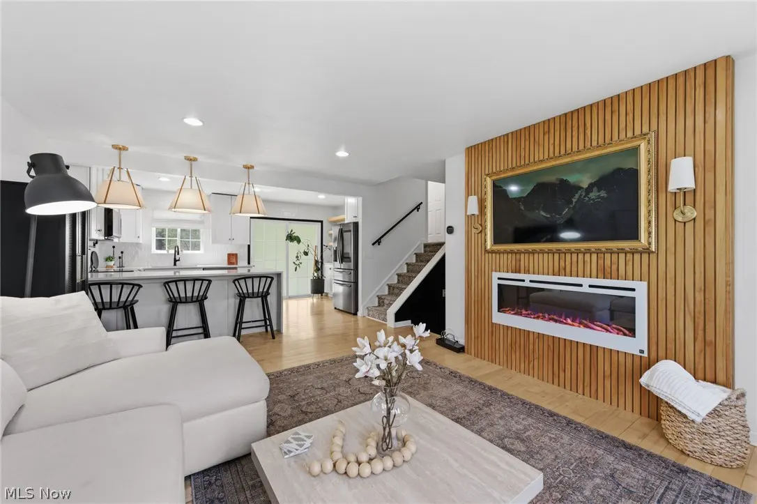 Open concept living space with a white sofa, kitchen island with black stools, and a wood-paneled wall with a fireplace and framed art.