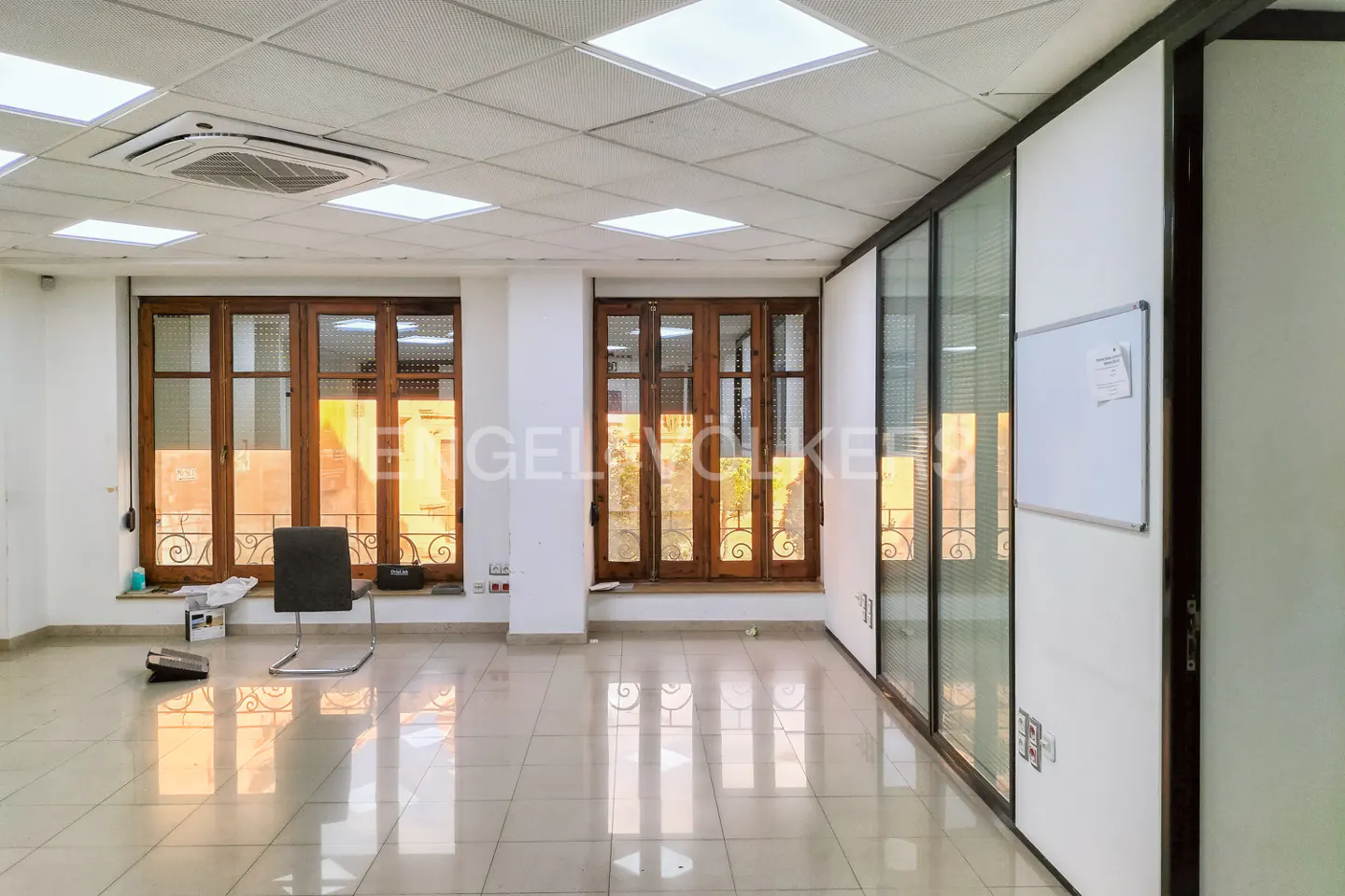 Bright office space with tiled floors, wood-framed windows, and glass-paneled walls. A chair sits near the window.