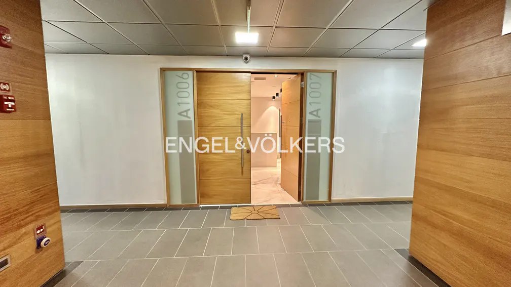 Hallway with gray tile floor, white walls, and wood doors labeled A1006 and A1007. A tan mat sits in front of the open doorway.