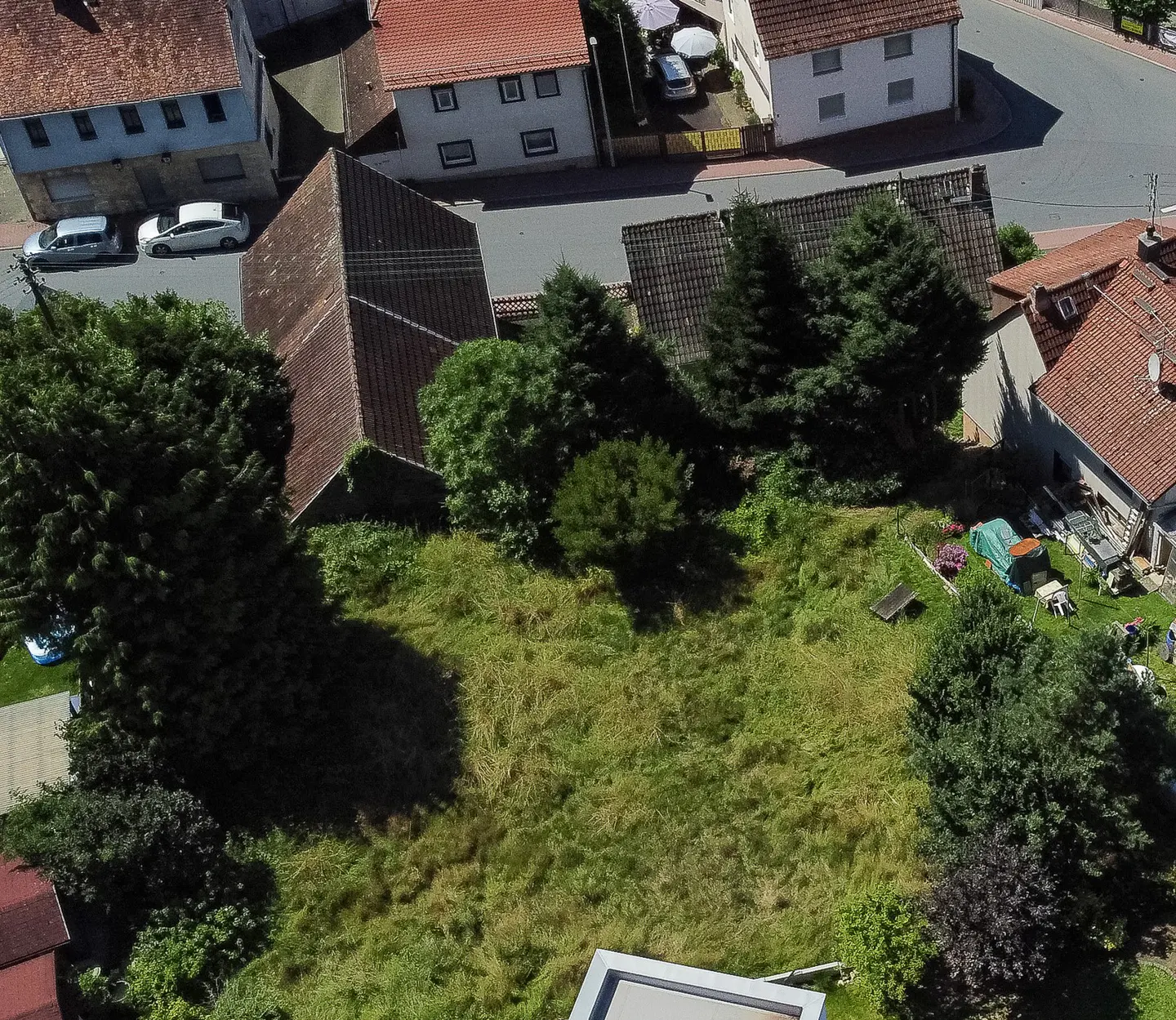 Aerial view of a grassy lot surrounded by houses and trees in a residential area.