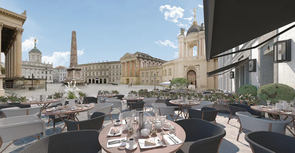 Outdoor cafe with tables and chairs, set against a backdrop of historic buildings and a blue sky.