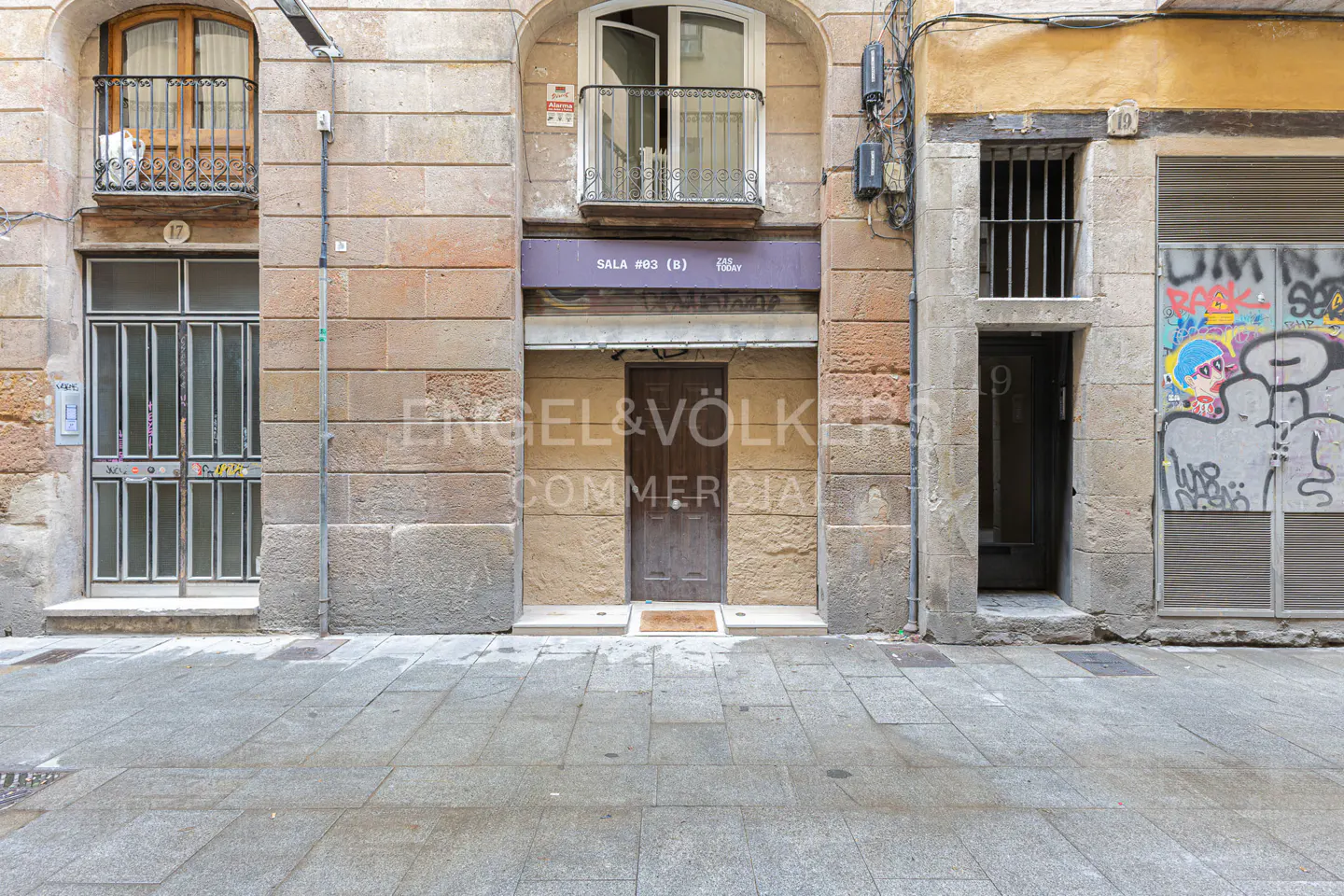 Exterior view of three stone buildings with doors and balconies on a city street.