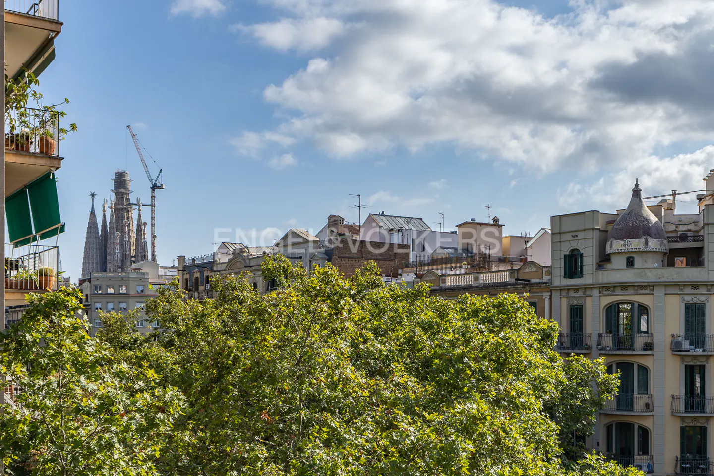View of Barcelona cityscape with Sagrada Familia, buildings, trees, and blue sky with clouds.