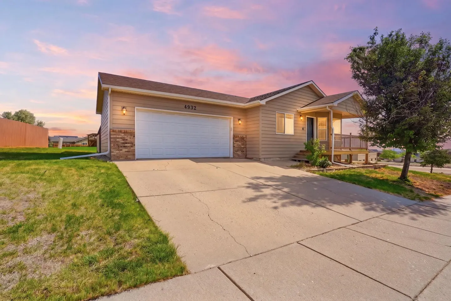 Tan single-story house with a two-car garage and front porch under a vibrant pink and orange sunset sky.