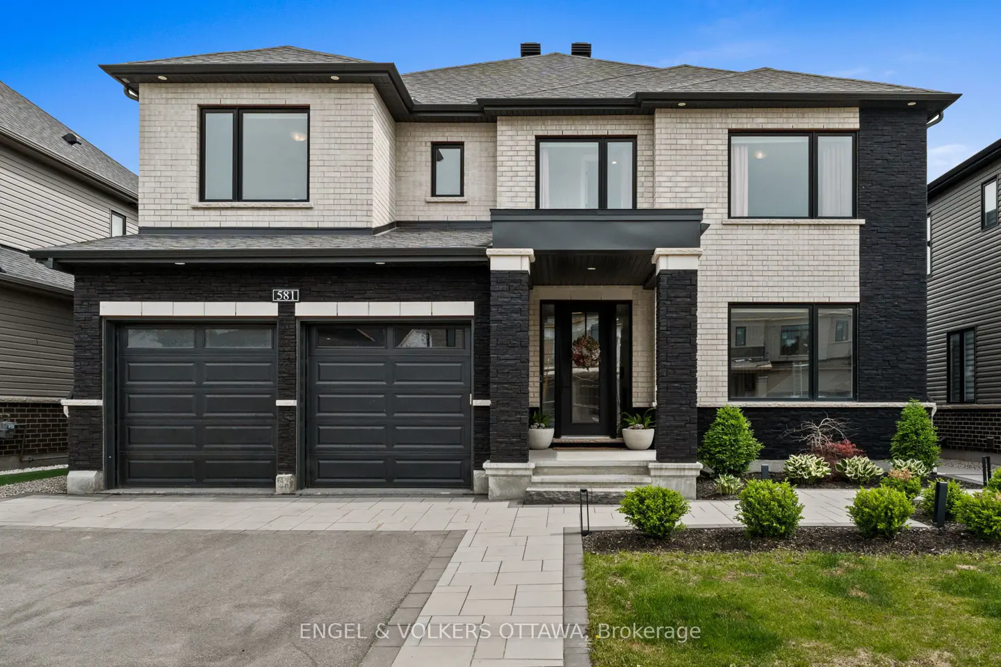 Modern two-story home with white brick and black stone accents, a double garage, and a paved walkway under a blue sky.