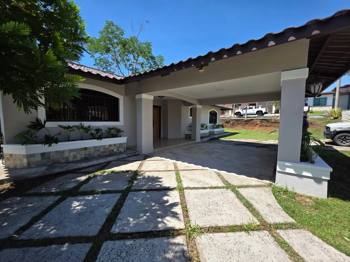 Beige house with a covered driveway and a tiled walkway on a sunny day.