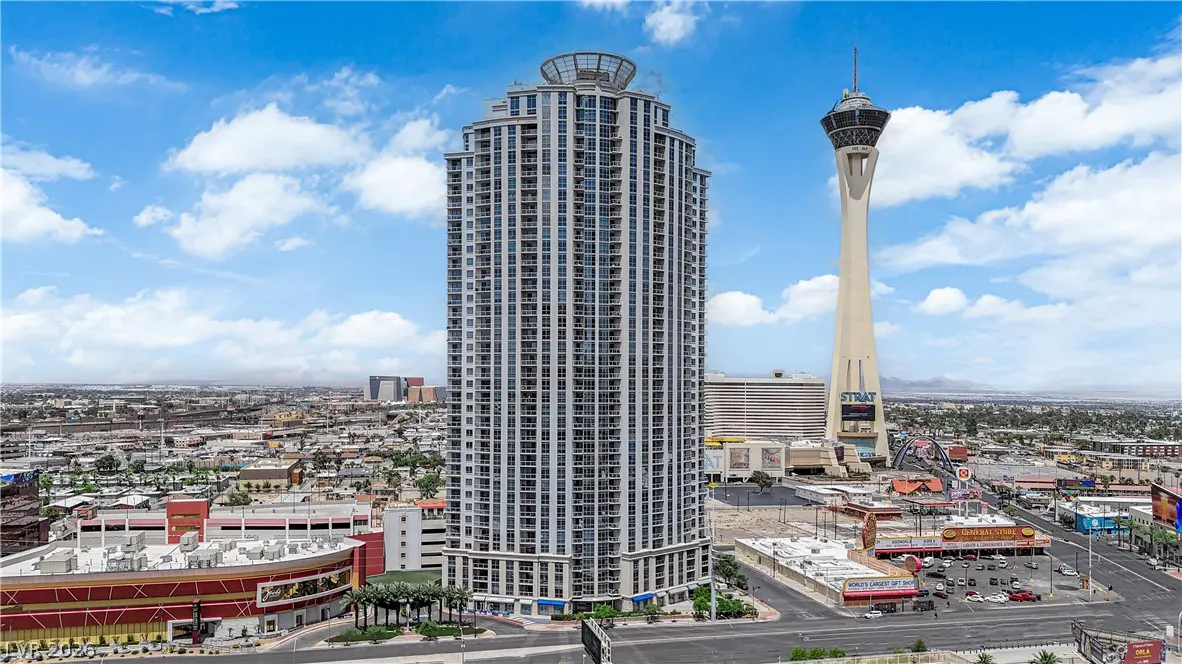 Las Vegas cityscape featuring a tall condo building and the Stratosphere tower under a blue, cloudy sky.