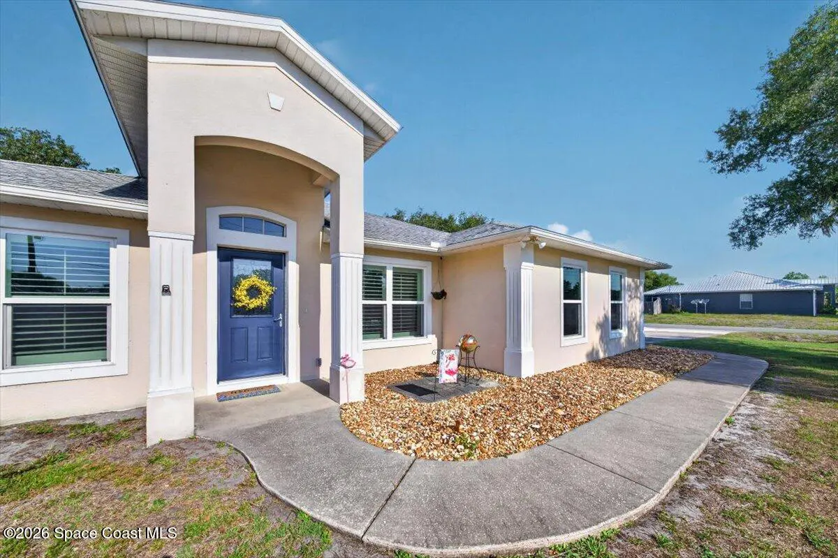 Beige house with a blue door and yellow wreath. A concrete walkway leads to the entrance. Windows have white trim.