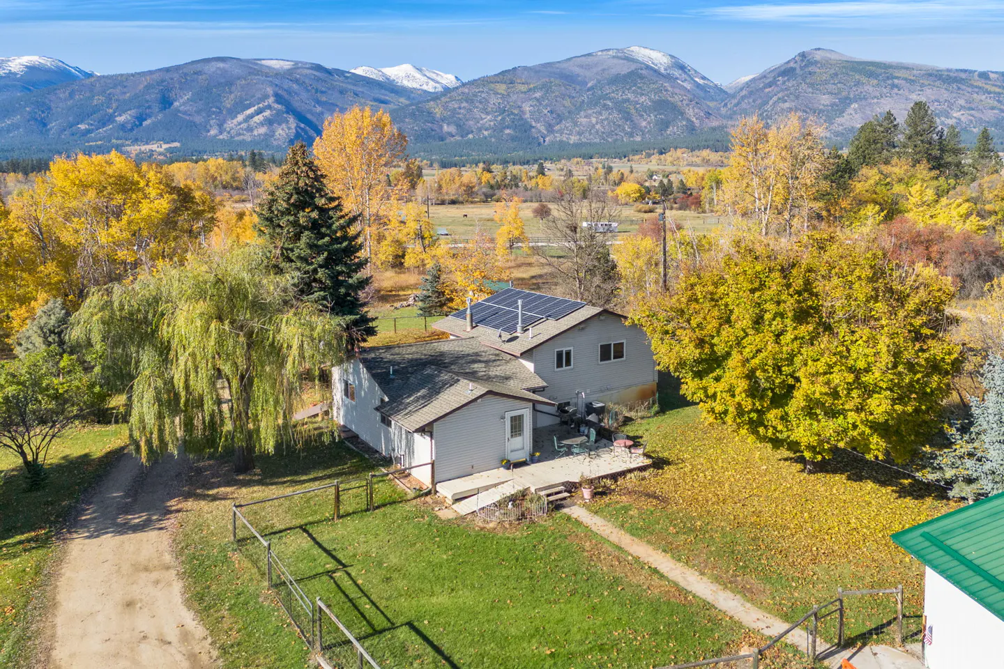 Aerial view of a gray house with solar panels, surrounded by fall foliage and mountains in the background.
