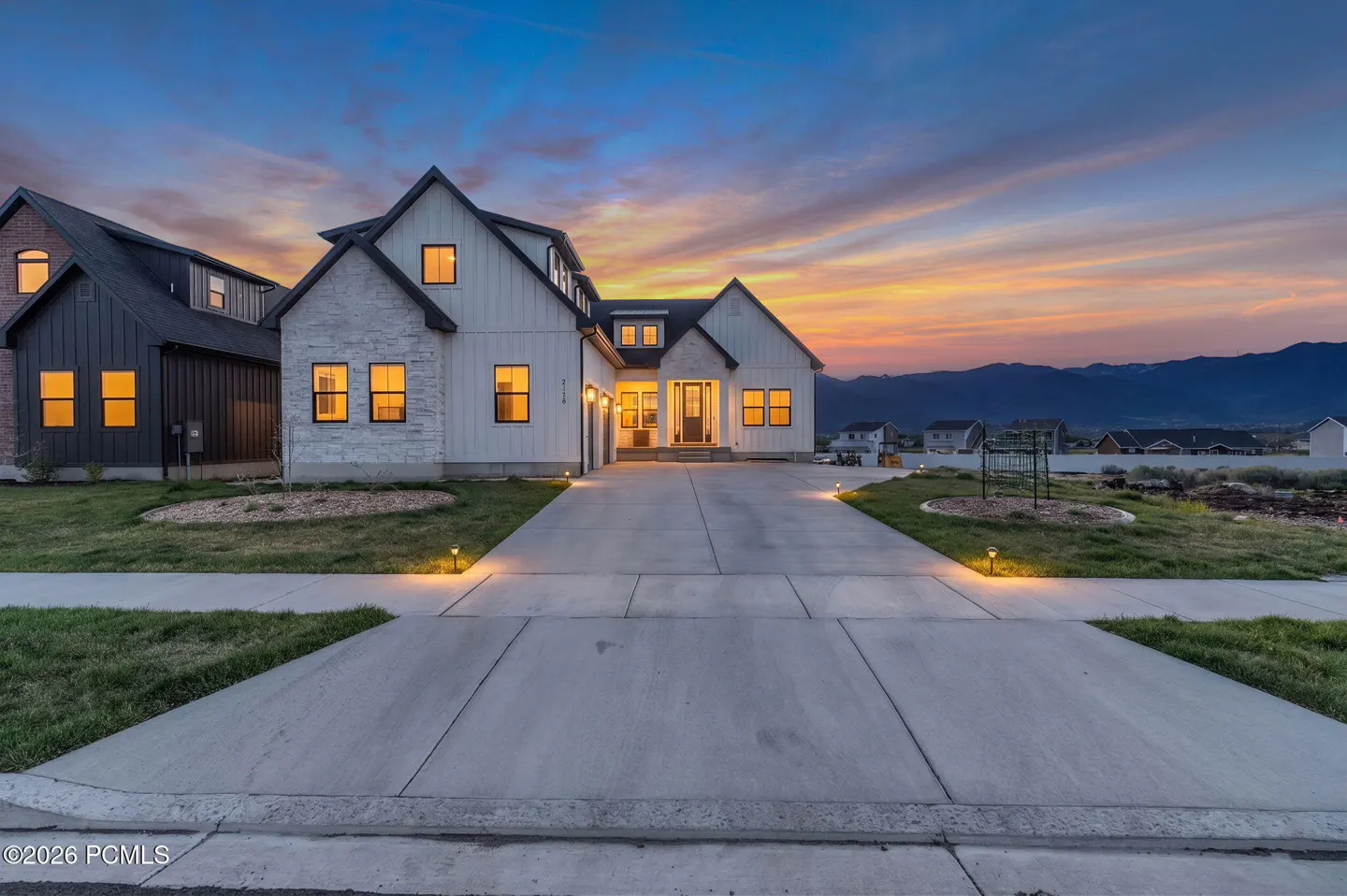 Exterior of a modern farmhouse-style home with a long driveway at dusk. The sky is a mix of orange, pink, and blue.