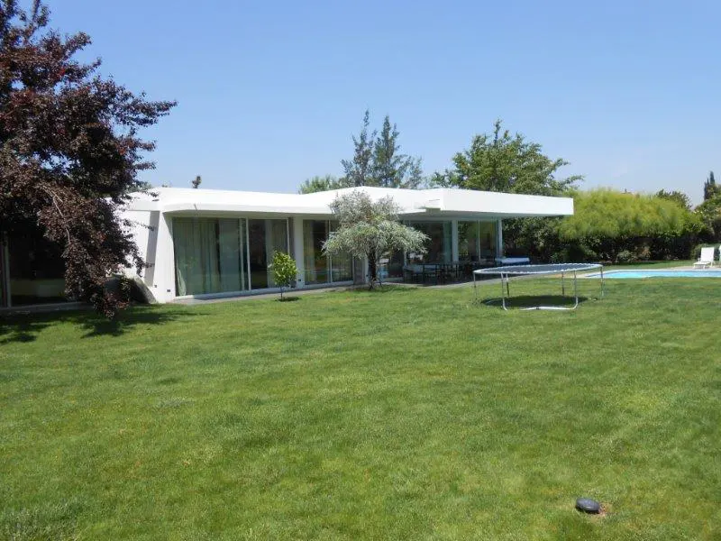Modern white house with large windows, green lawn, and trampoline. Blue sky above.