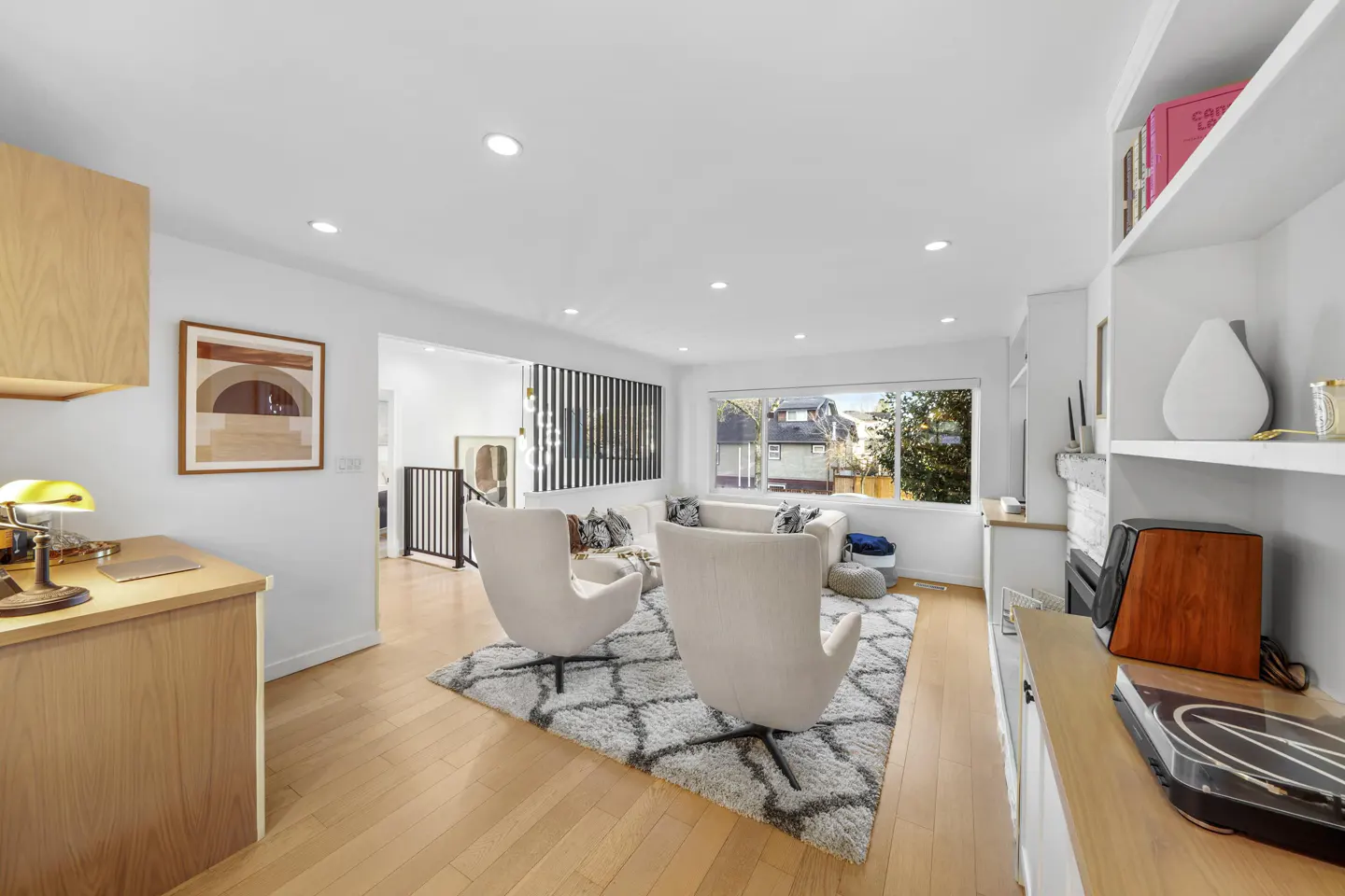 Bright, open living room with hardwood floors, white walls, and modern furniture. Two white chairs face a white sofa near a large window.