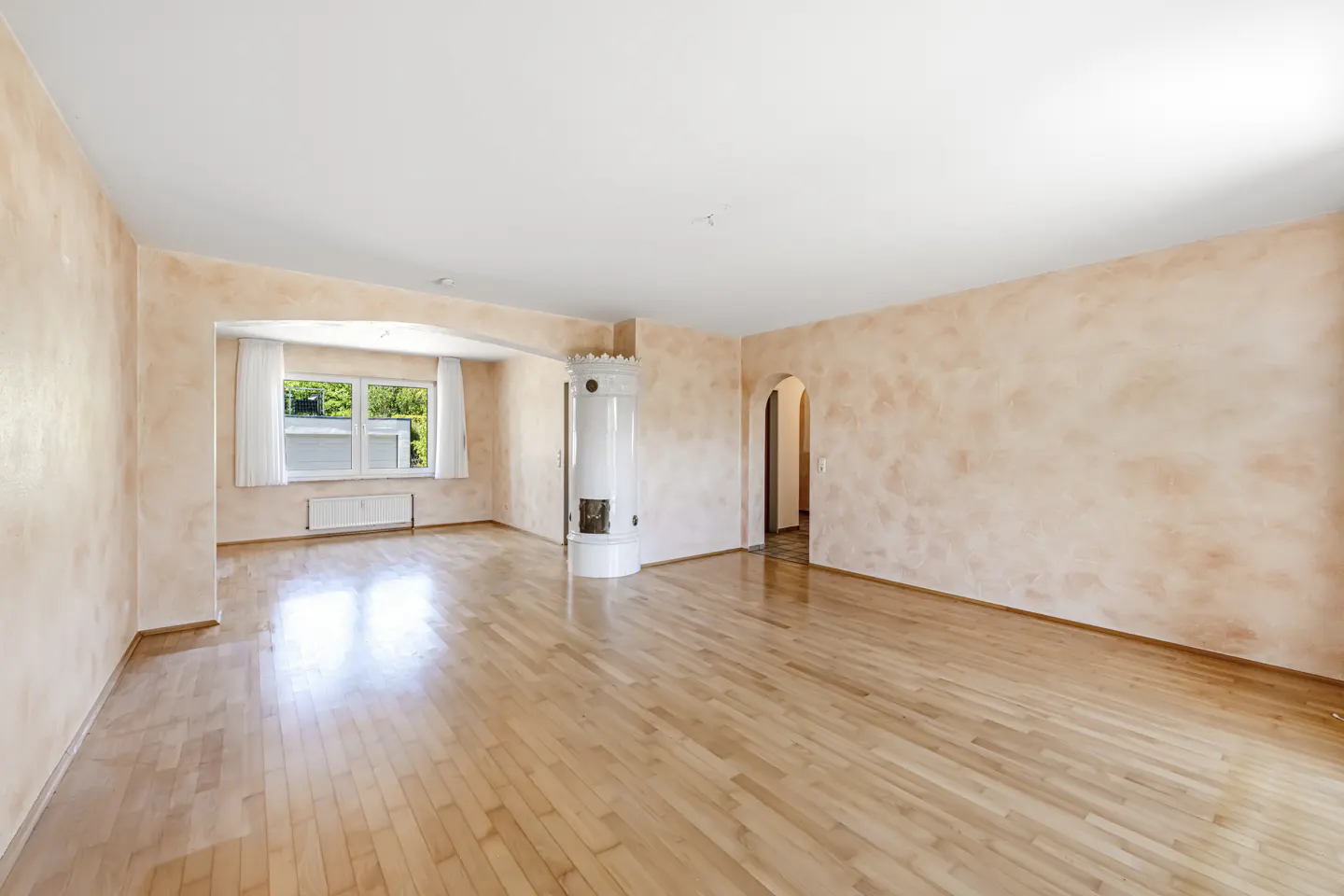 Empty living room with light wood floors, peach walls, a white fireplace, and a window with white curtains.