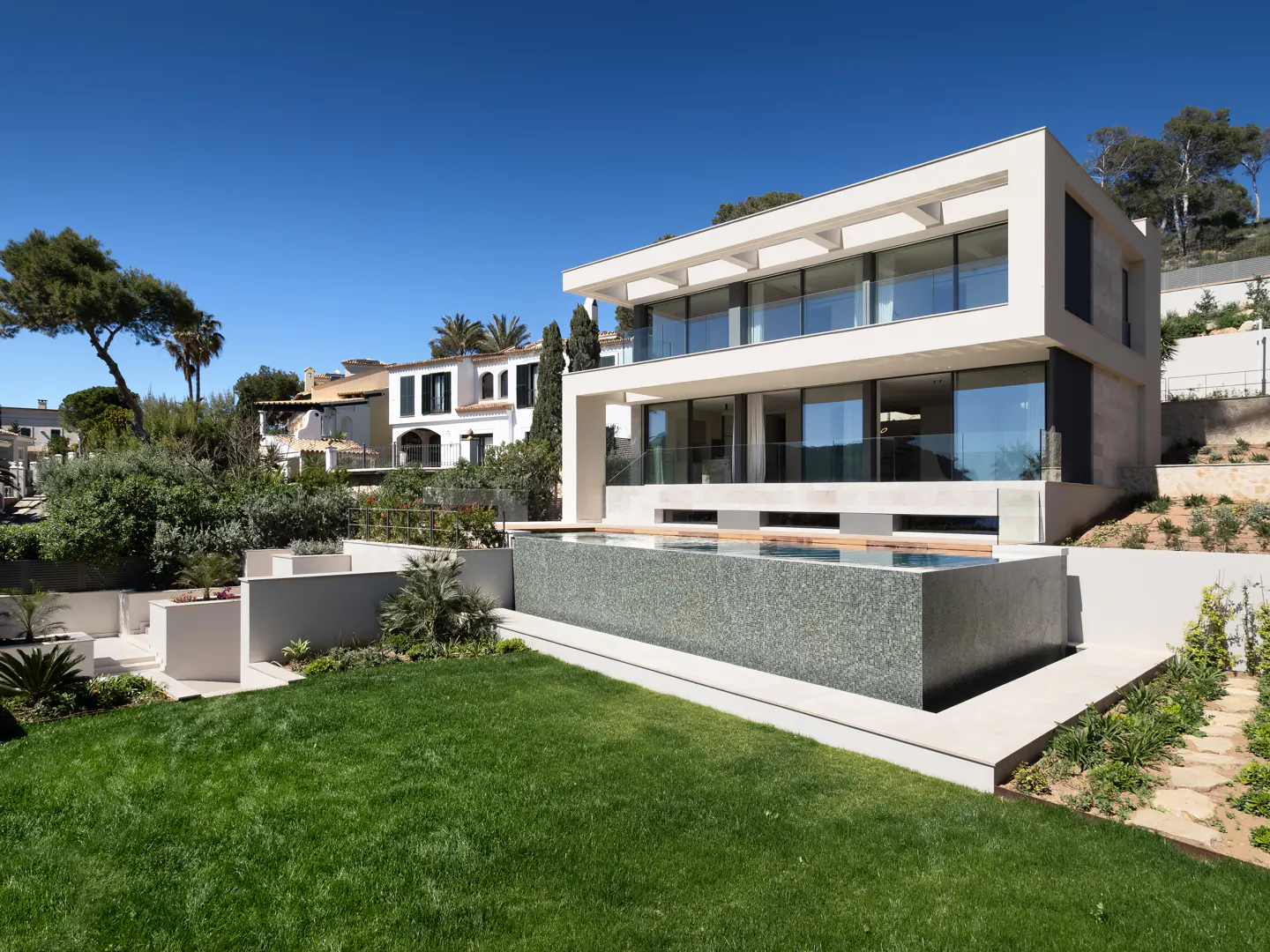 Modern two-story white house with large windows and a pool overlooking a green lawn on a sunny day.
