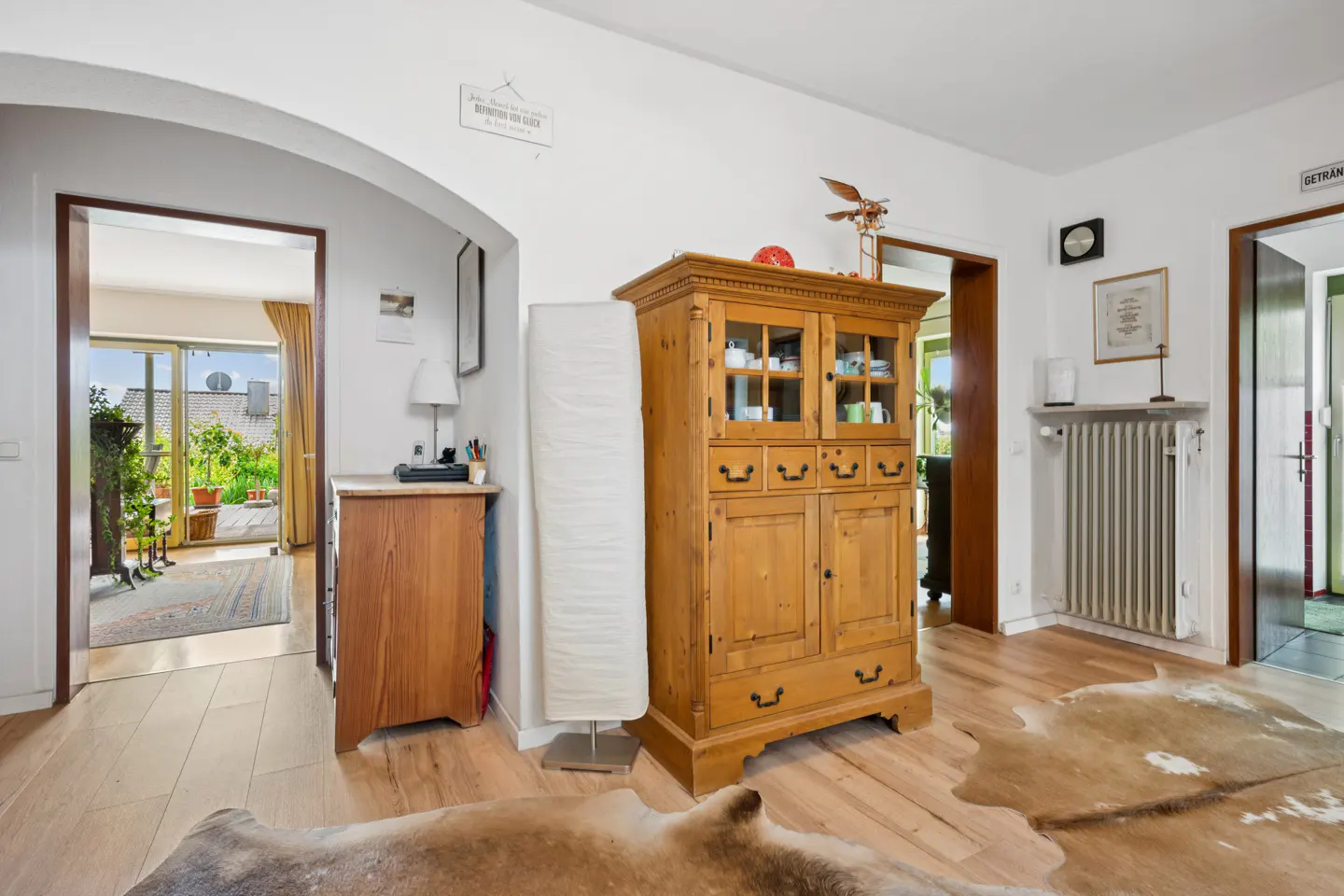 Interior view of a home with light wood floors, a large wooden cabinet, and doorways leading to other rooms and a patio.