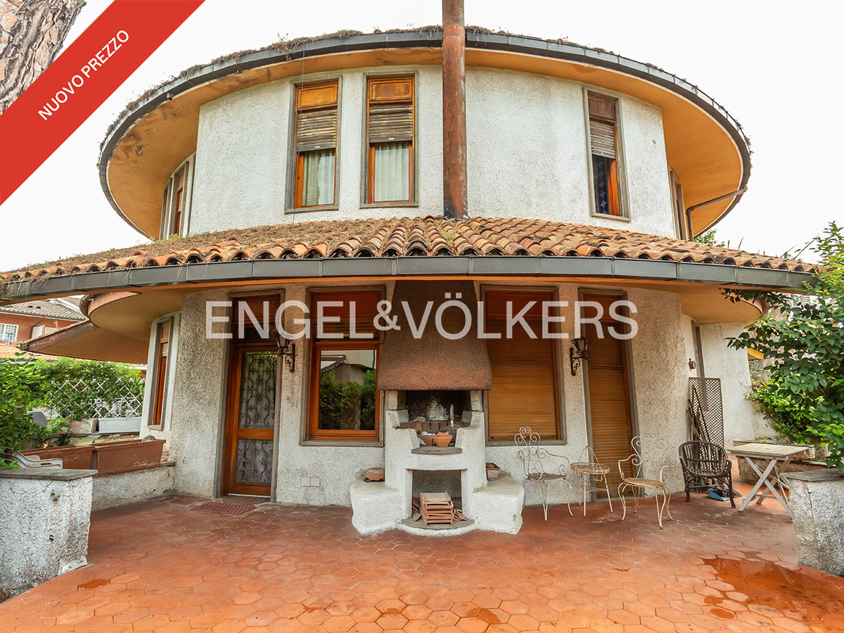 Exterior of a unique circular house with a terracotta tiled patio, outdoor fireplace, and patio furniture.