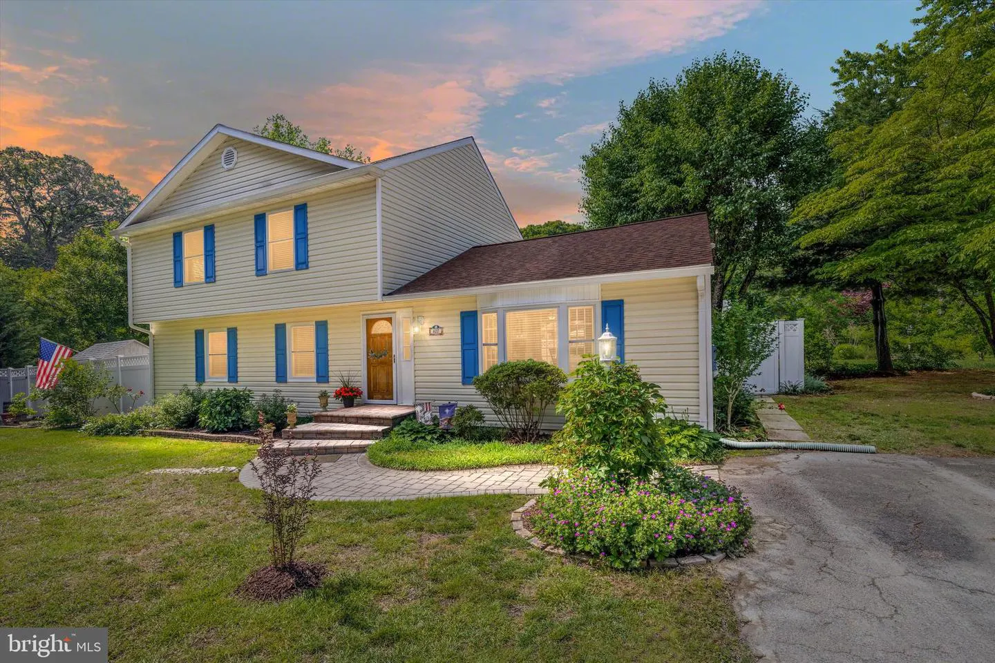 Two-story home with yellow siding and blue shutters. A brick walkway leads to the front door. Green trees surround the house.