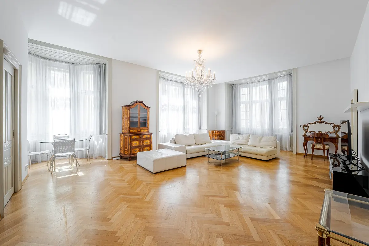 Bright living room with herringbone wood floors, white sofa, glass table, chandelier, and antique cabinet.