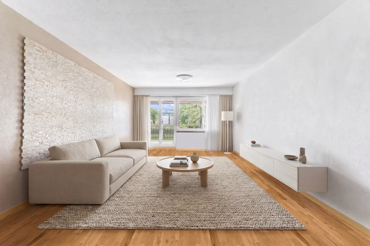 Bright living room with a beige sofa, round coffee table on a woven rug, and a white stone accent wall. A balcony door leads to a green view.