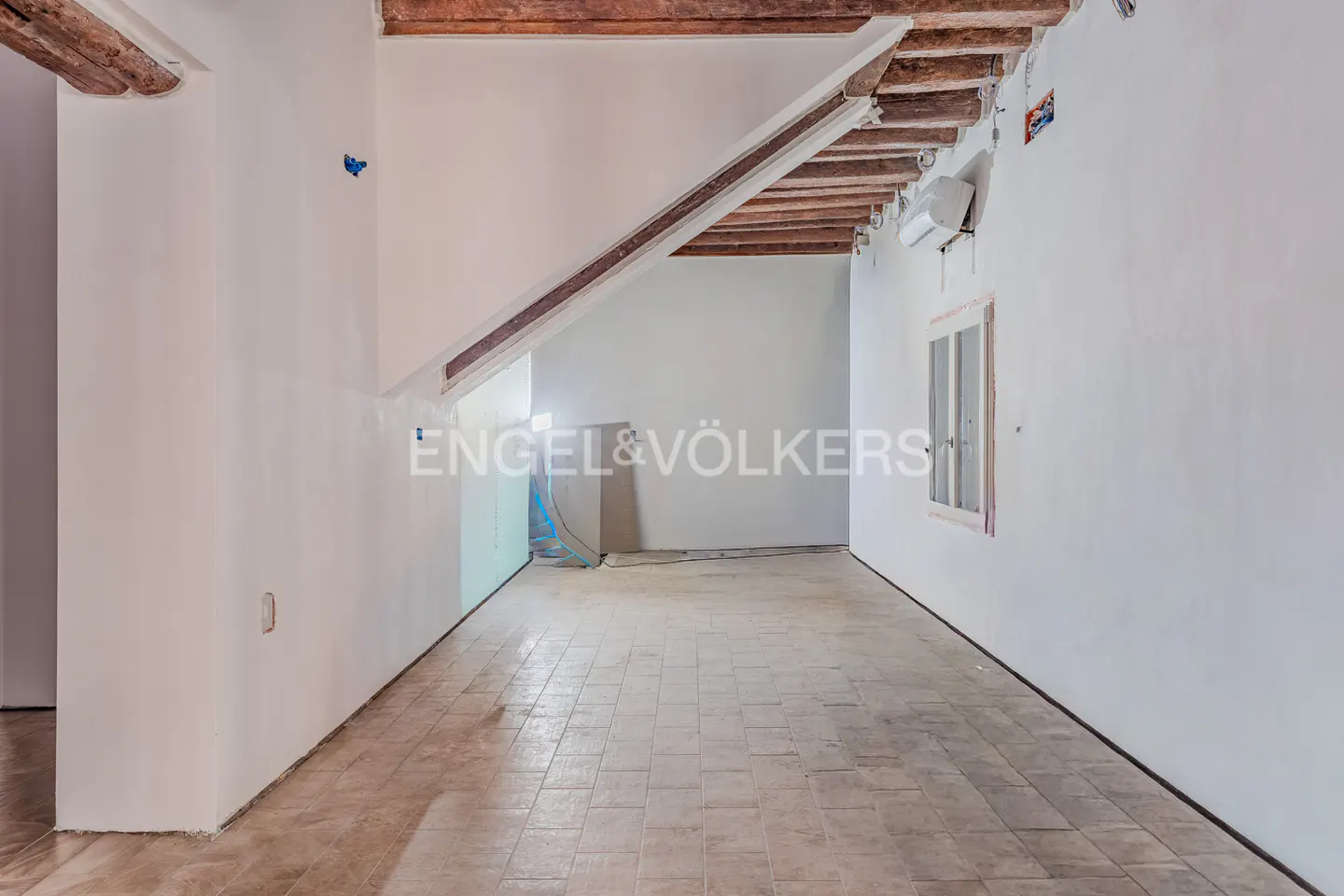 Empty room with white walls, tile floor, and exposed wood beams on the ceiling. A window is on the right wall.